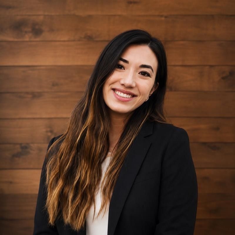 Woman in blue shirt smiles in front of a wooden fence.