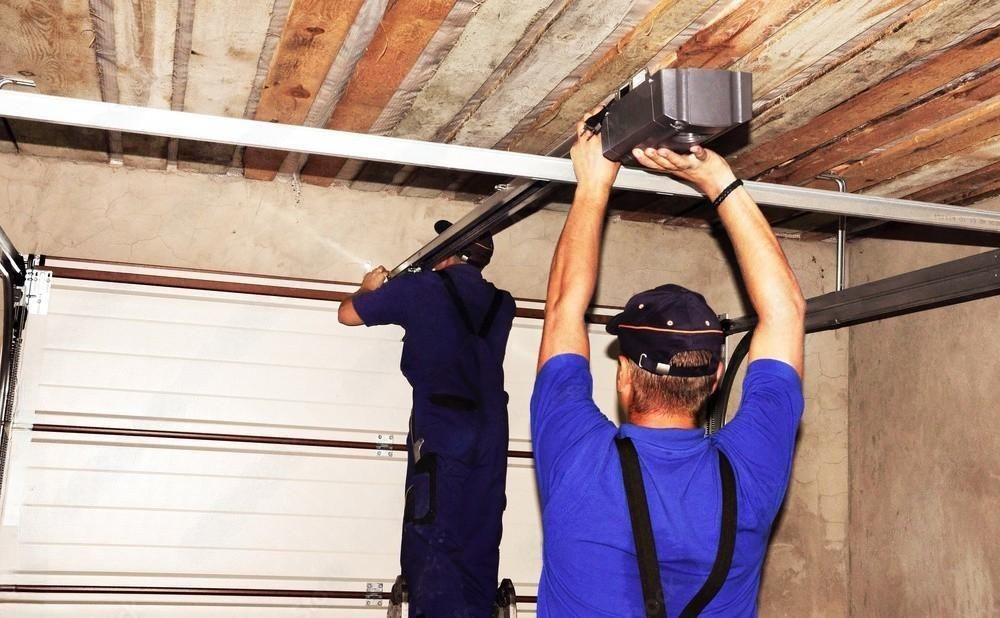 two men are working on a garage door in a garage .