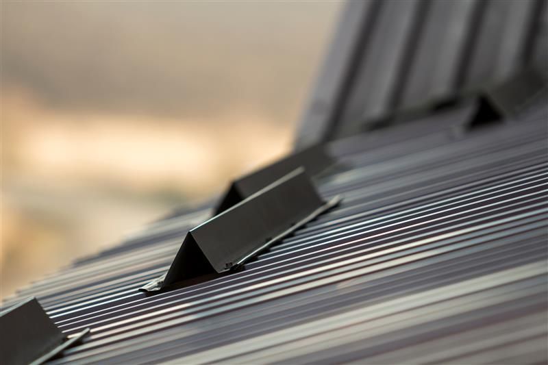 Close-up of a dark metal roof with several small, angled metal brackets spaced across its surface.