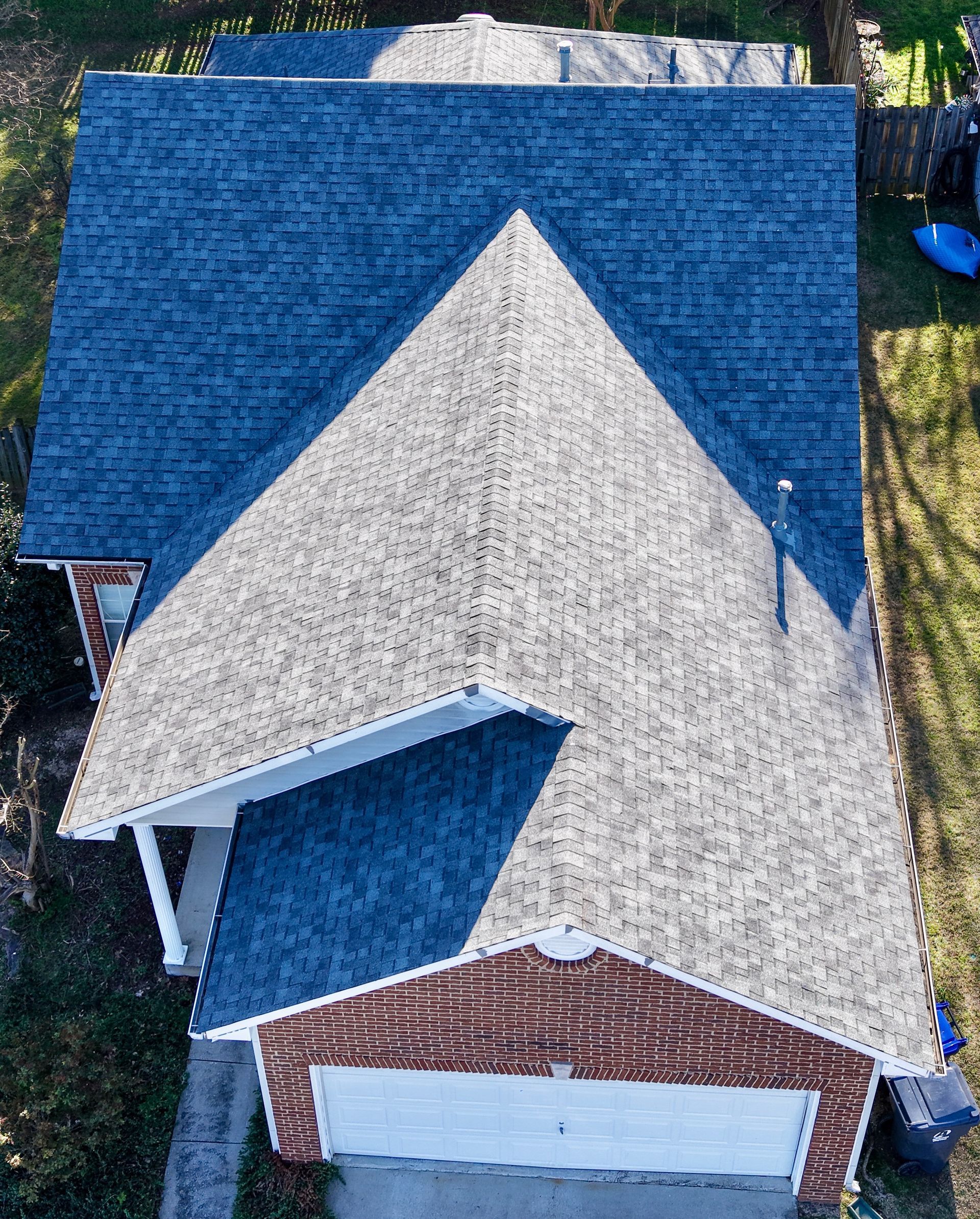 An aerial, overhead view of a house roof with mixed blue, tan, and brown shingles, and a white garage door below.