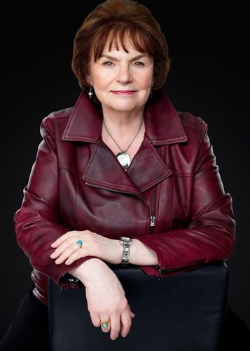 Portrait of a person in a burgundy jacket, seated against a black background, smiling gently.