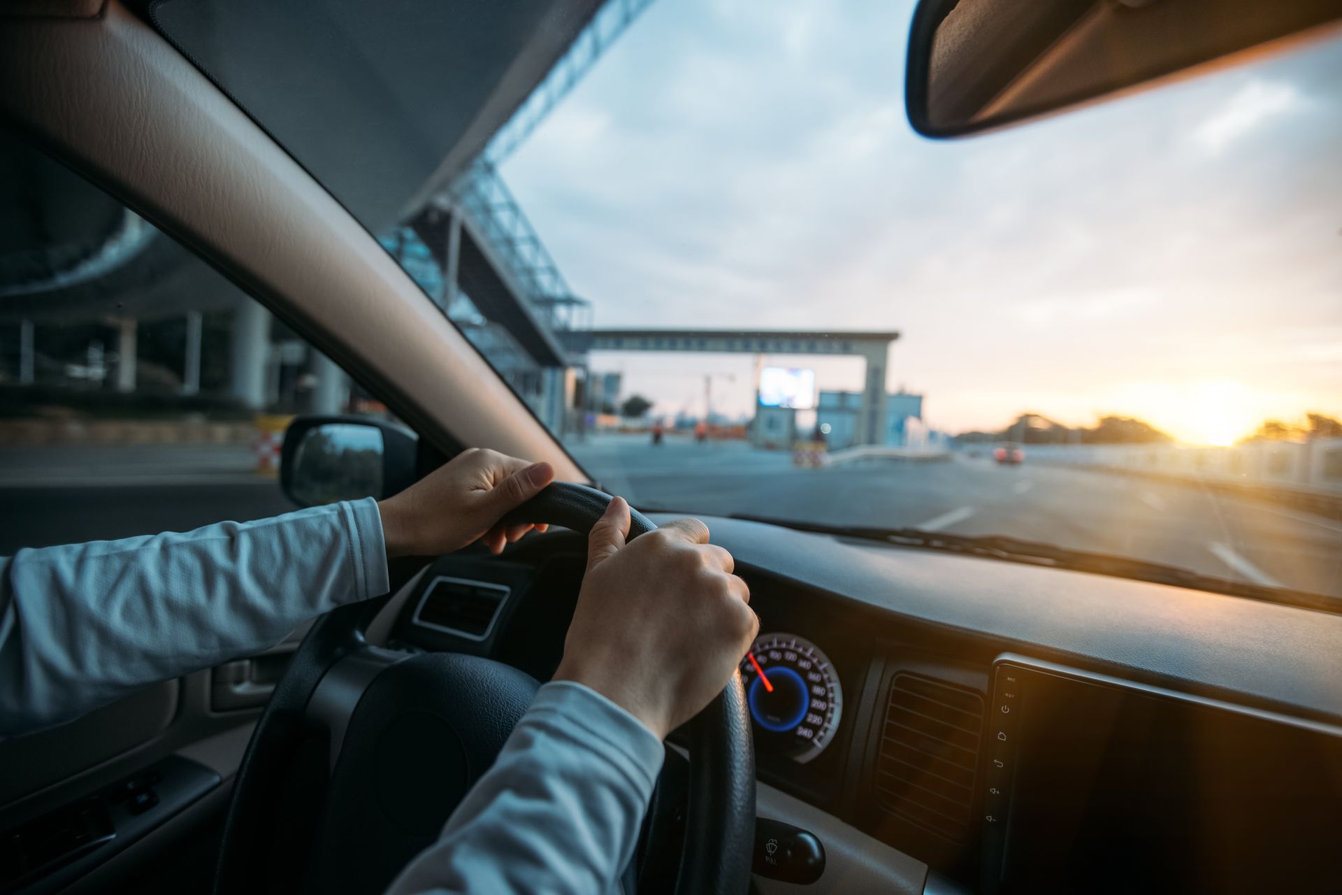 Driver holding the steering wheel inside a car at sunset on a highway.