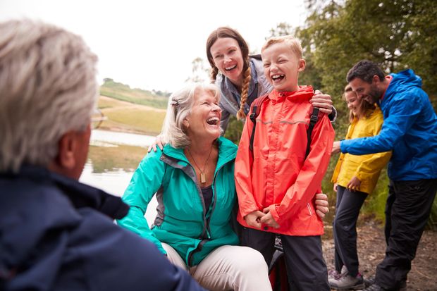 Group of smiling people in colorful jackets outdoors, chatting and laughing together by a grassy field
