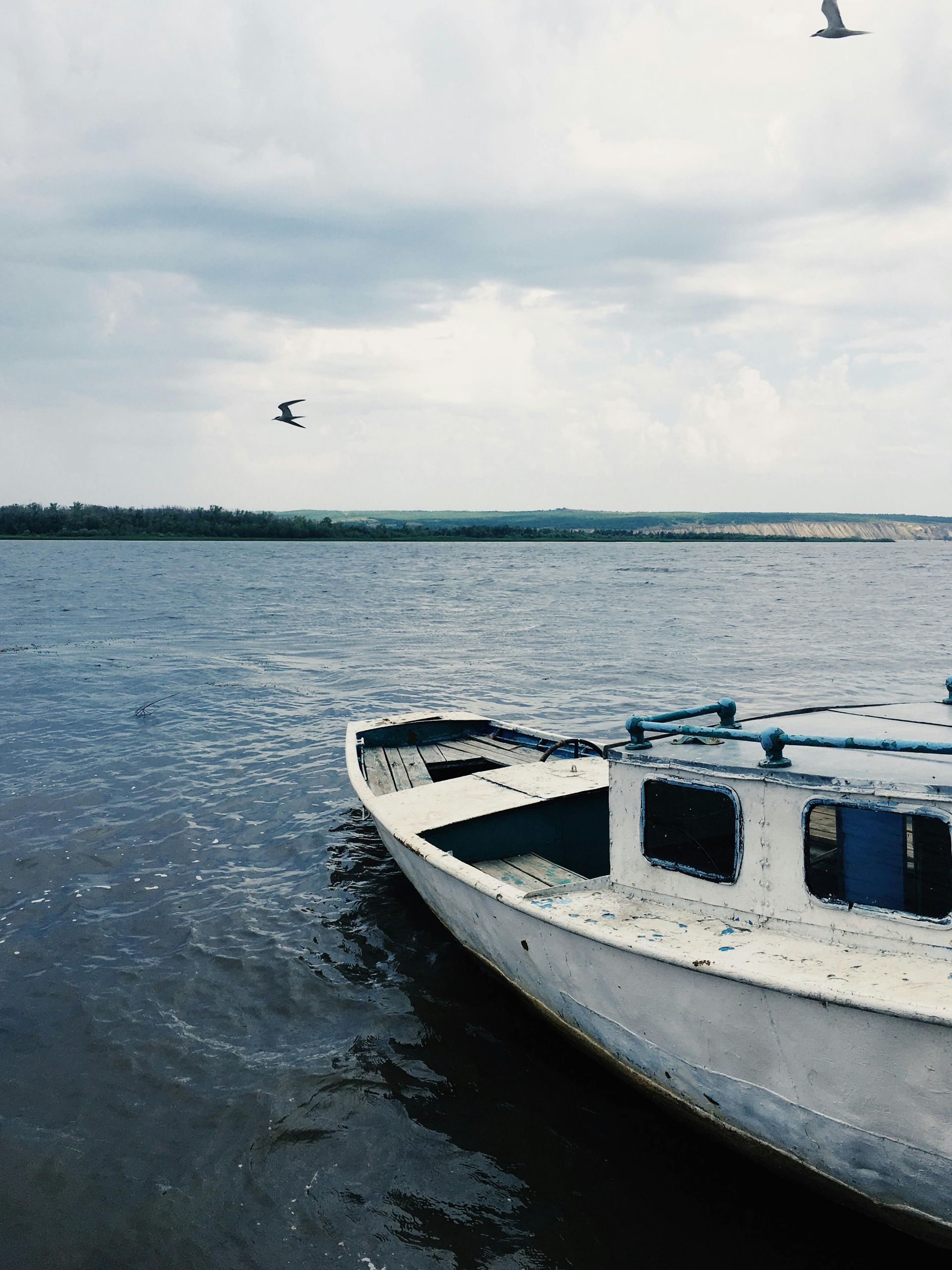 White boat on a calm lake with birds flying overhead and a cloudy sky