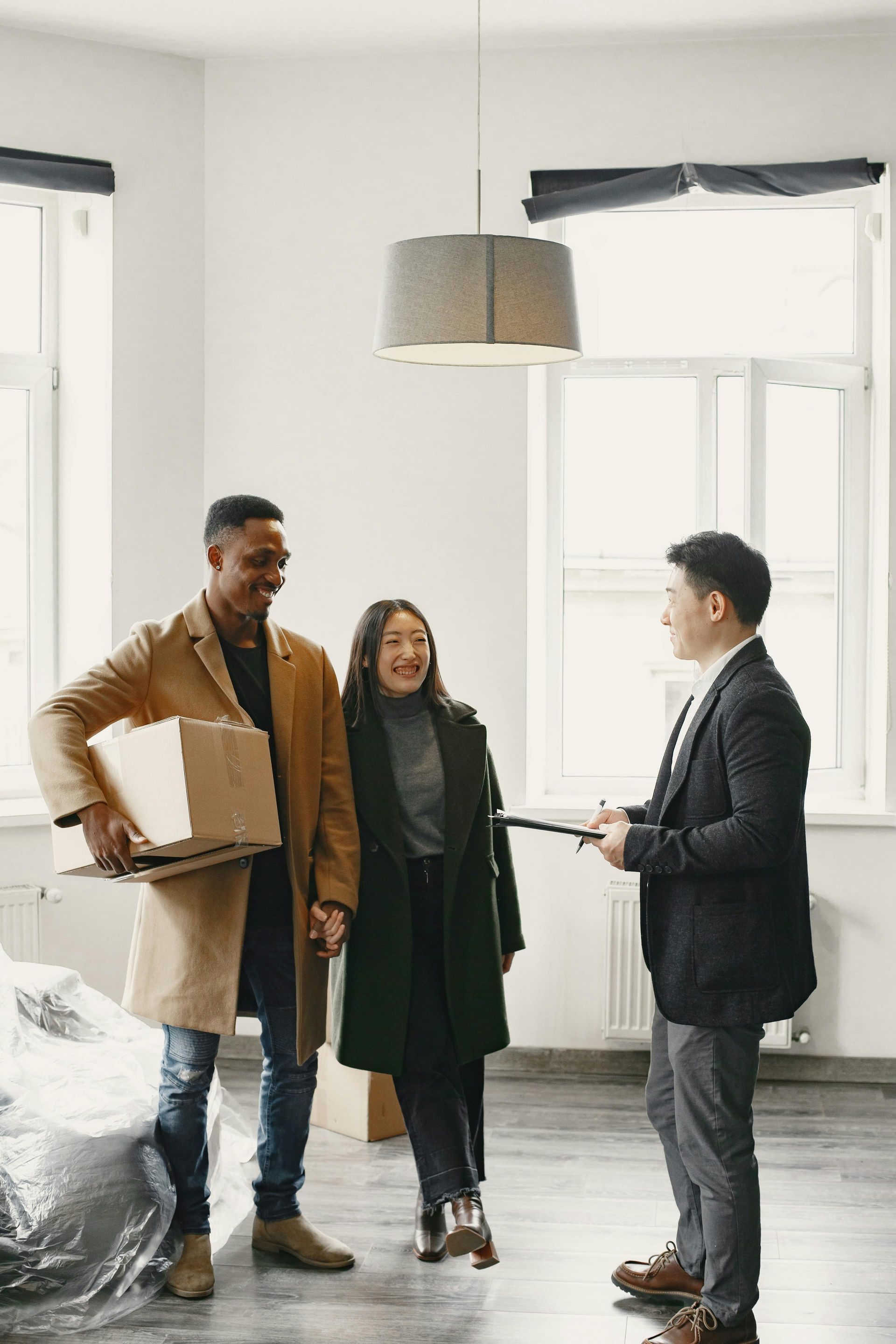 Three people talking in a bright, empty room with moving boxes and a window.
