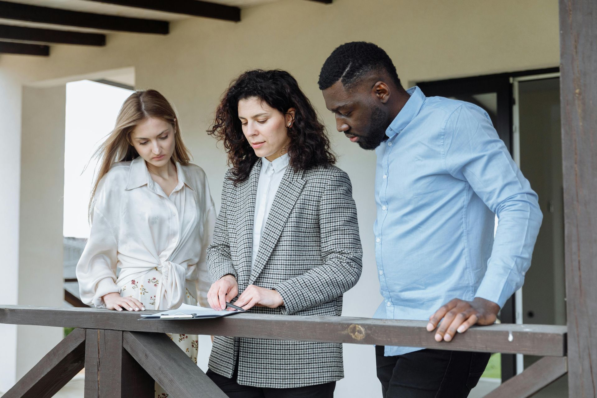 Three coworkers reviewing plans together on a balcony, leaning over a railing in a modern building.