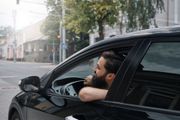 Man leaning out of a black car window on a rainy city street