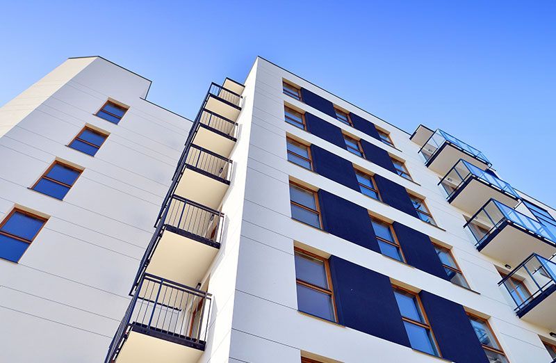 Low-angle view of a modern white apartment building with dark windows and balconies against a blue sky