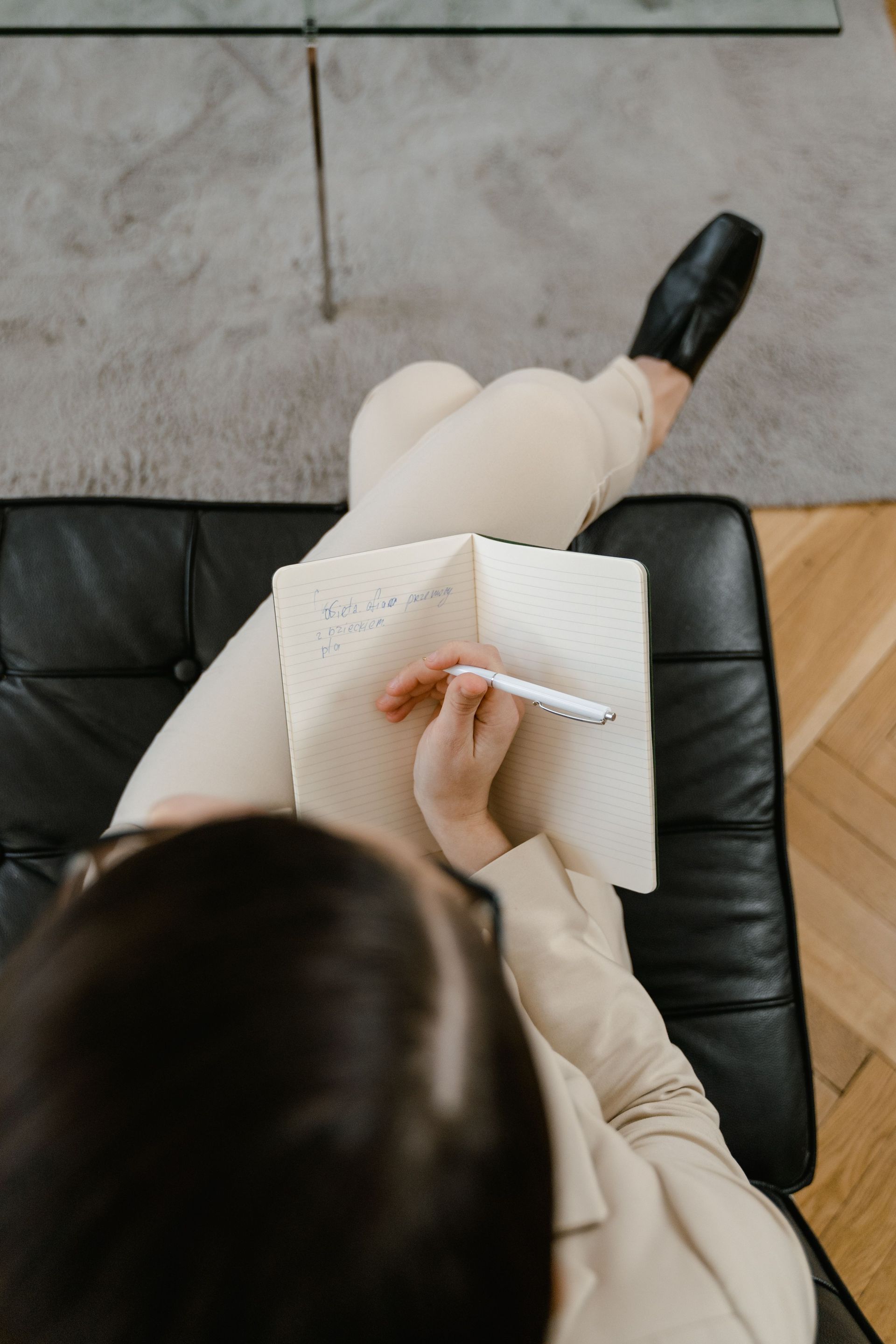 Woman writing in a notebook, looking down thoughtfully in soft natural light.