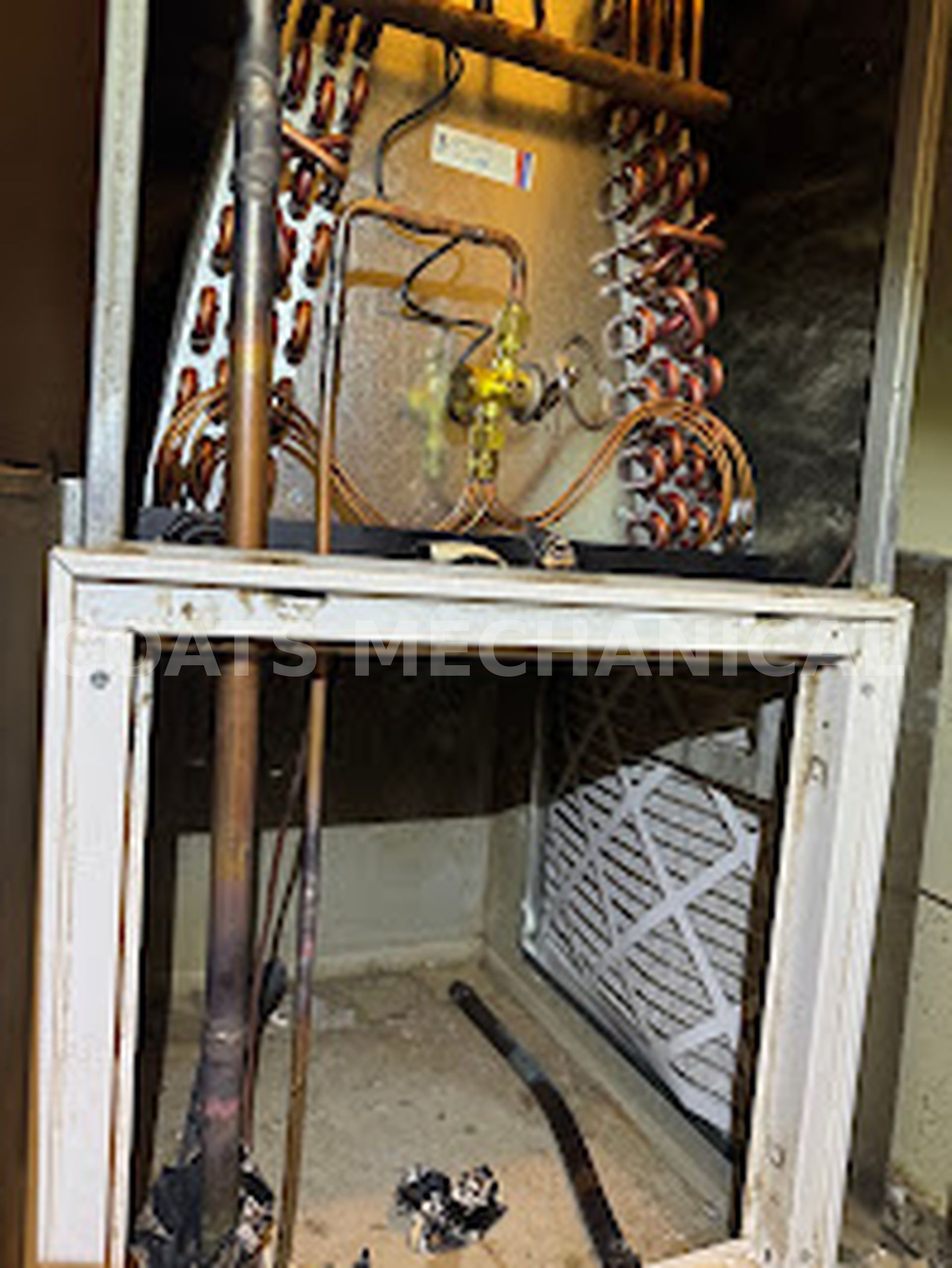 An HVAC indoor evaporator coil unit with exposed copper piping and an air filter installed in the lower housing section.