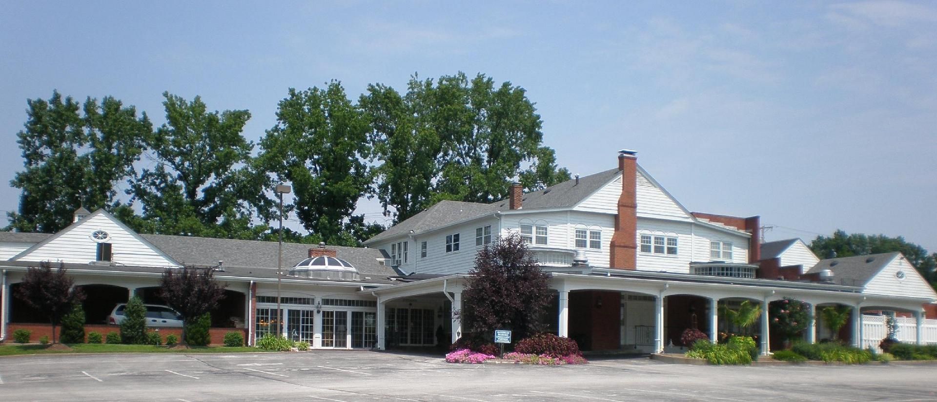 Single-story white storefronts with a red-brick chimney, trees, and a parking lot in front