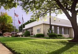Single-story brick office building with flags, trees, and a manicured lawn