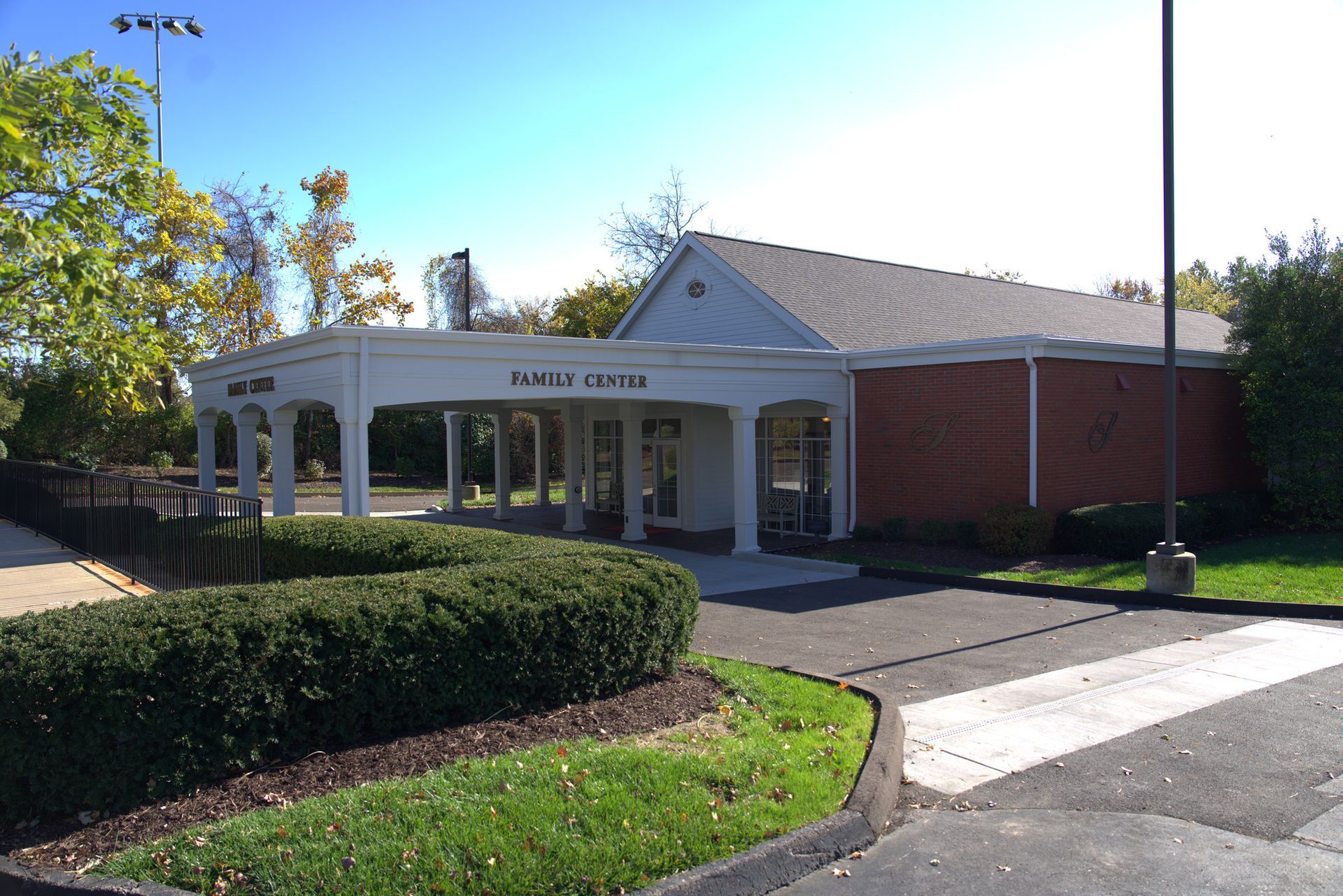 Small brick community building with white porch, glass doors, and landscaped entrance under a blue sky
