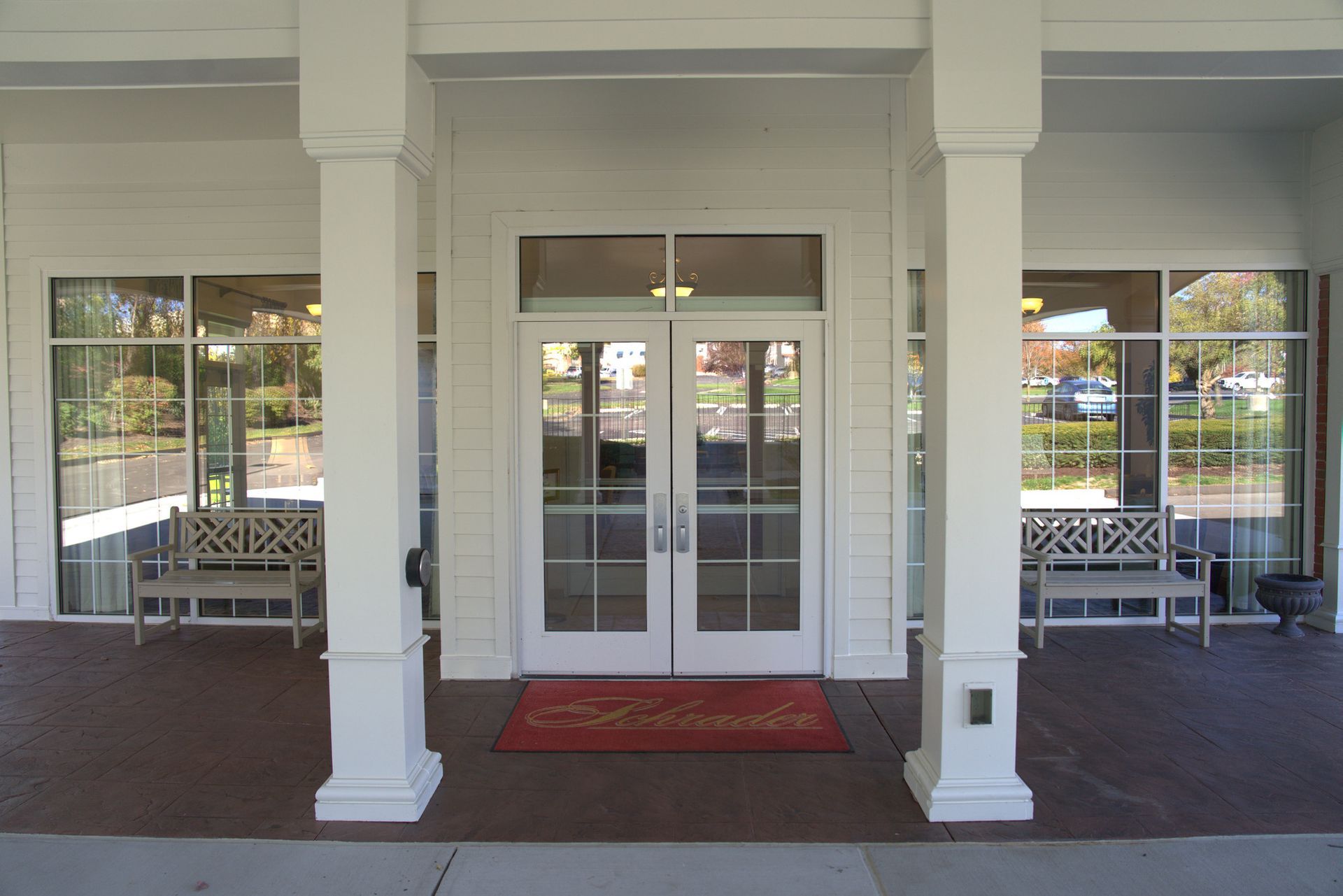 Front entrance with white columns, glass double doors, and red welcome mat on a covered porch.