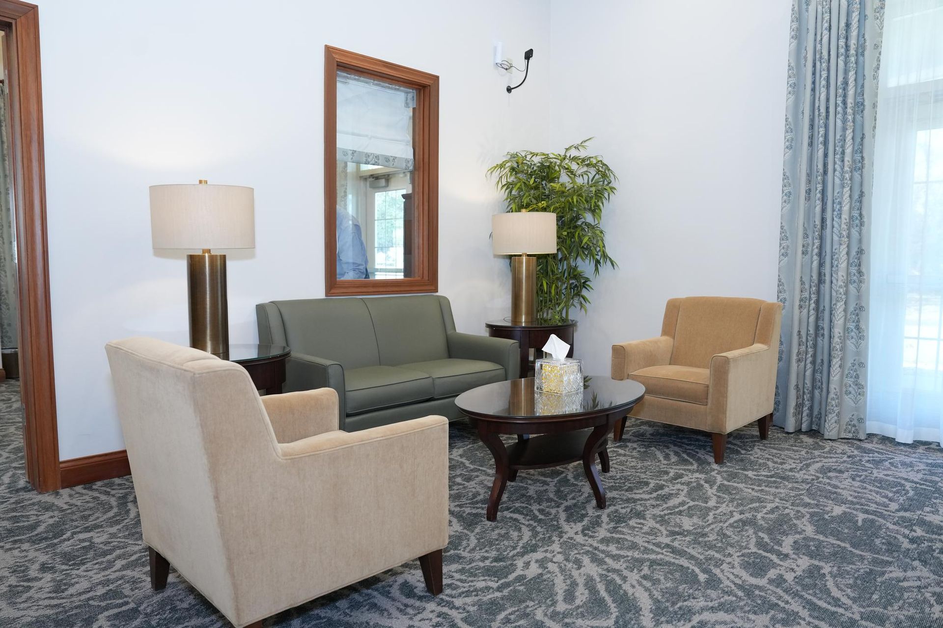 Cozy living room with beige and green chairs, round coffee table, lamp, mirror, plant, and blue patterned rug