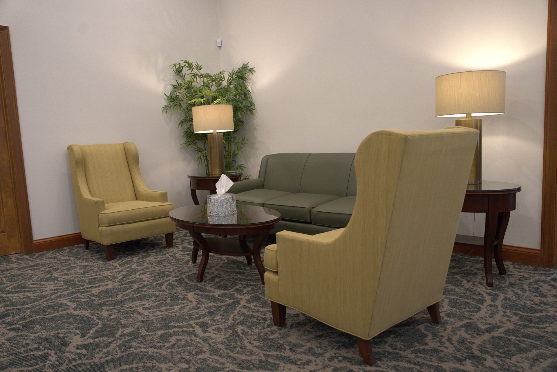 Quiet living room with beige chairs, green sofa, wooden tables, lamp, and patterned carpet.