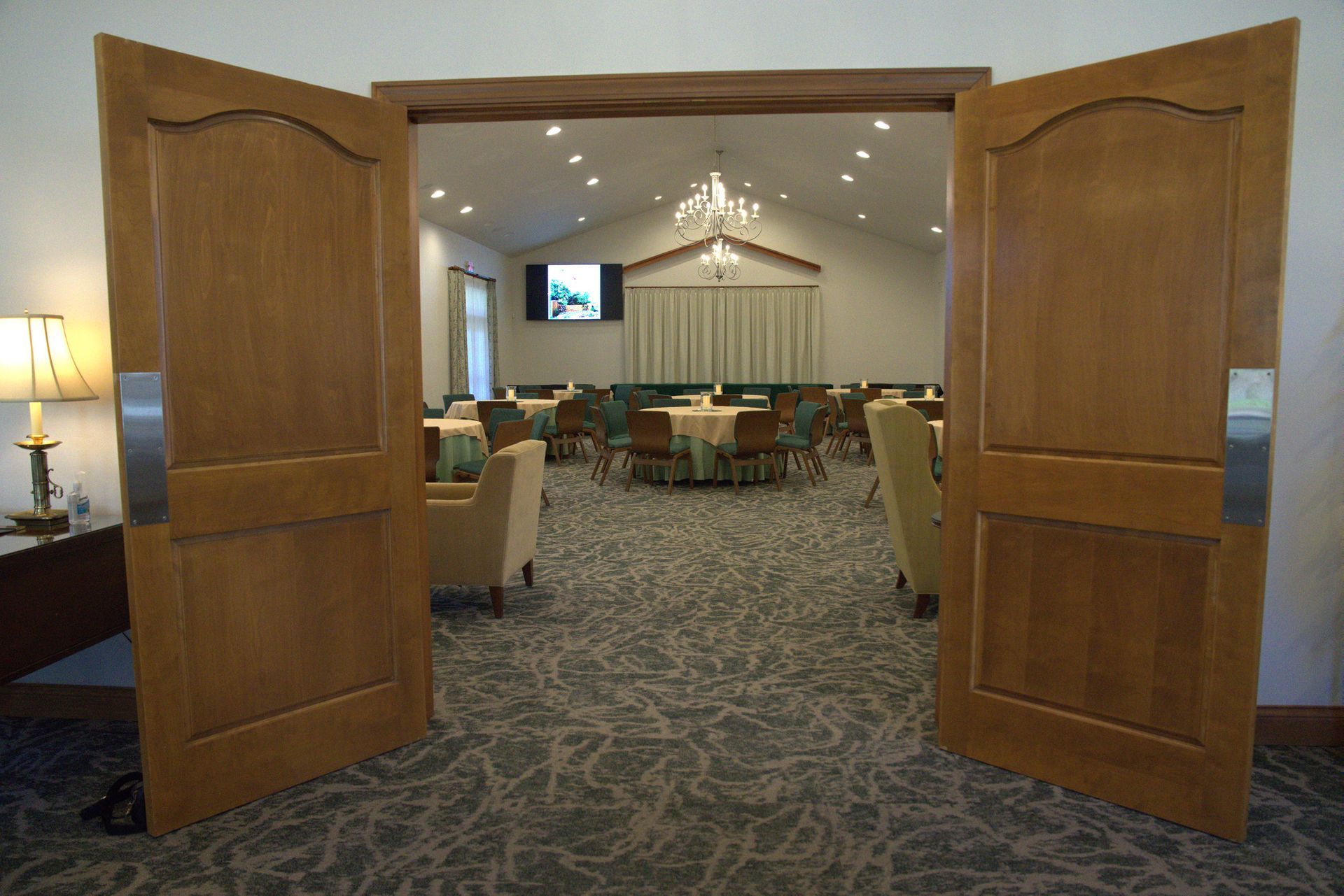 Open double wooden doors leading into a carpeted conference room with tables, chairs, and a chandelier.