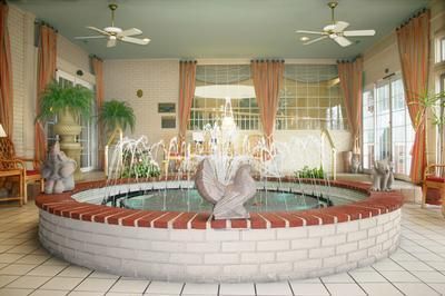 Indoor spa with circular hot tub, tiled floor, potted palms, curtains, and ceiling fans