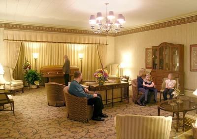 Elegant hotel lounge with armchairs, chandelier, and several people seated near a table with flowers