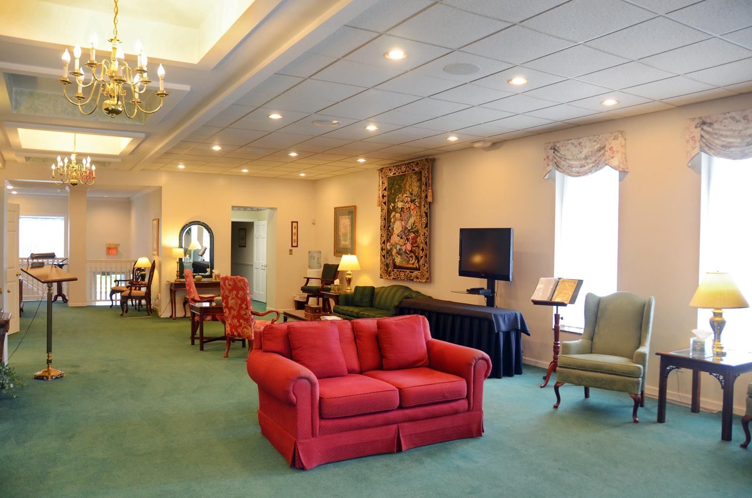 Bright lounge with green carpet, red sofa, chairs, lamps, and framed wall art
