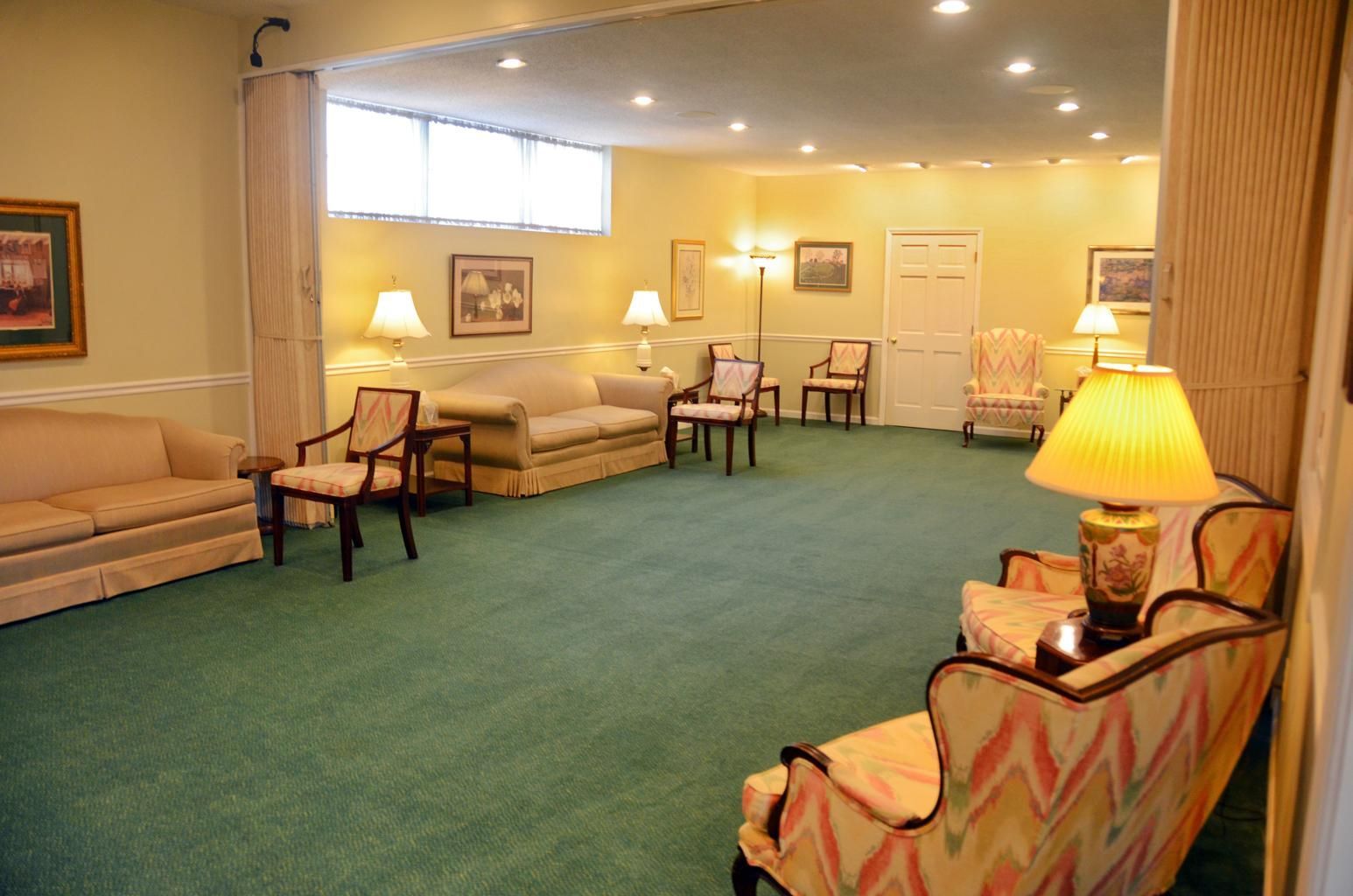 Empty hotel lounge with green carpet, cream sofas, and warm table lamps
