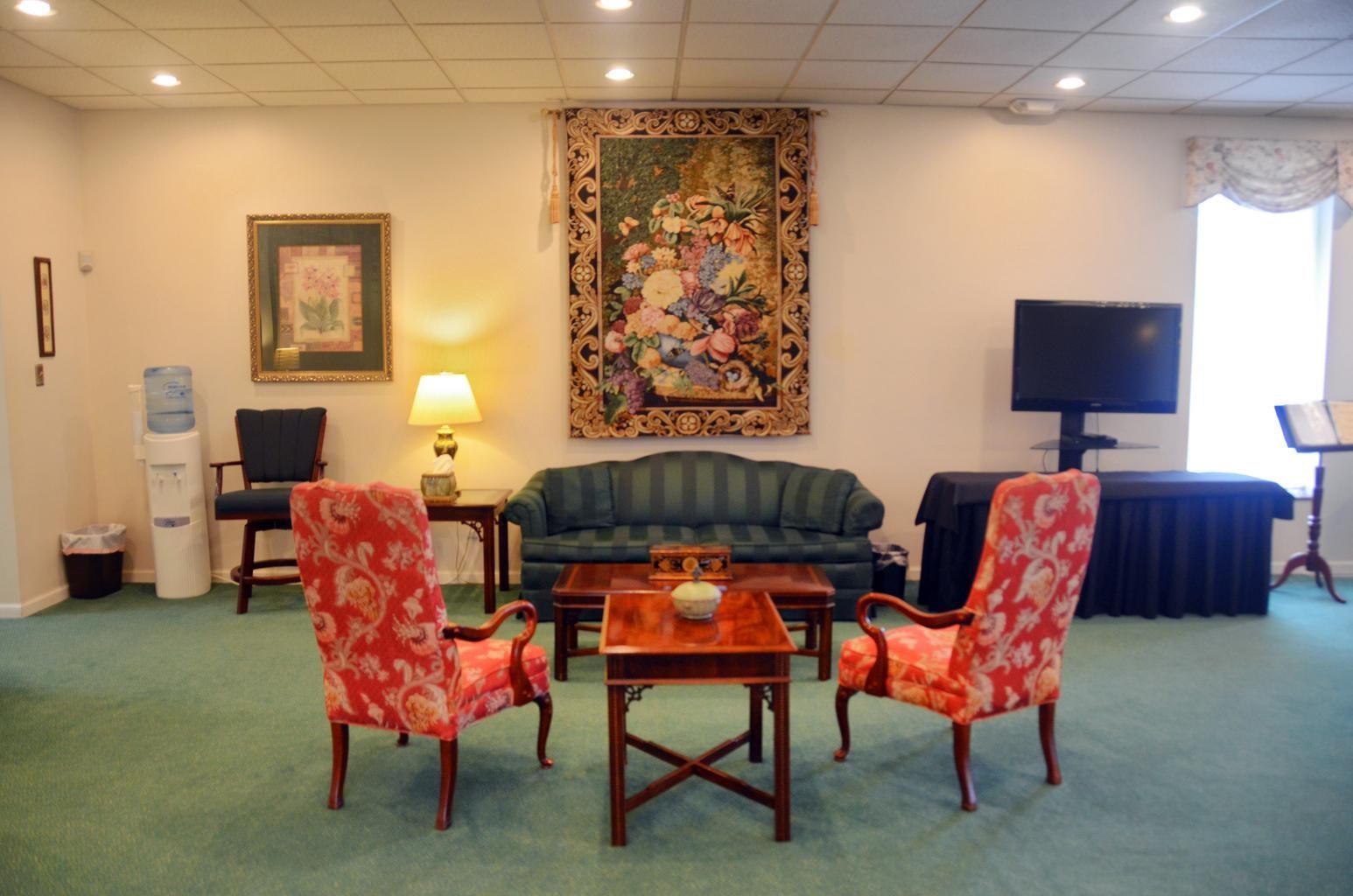 Living room with green sofa, floral chairs, lamp, TV, and turquoise carpet