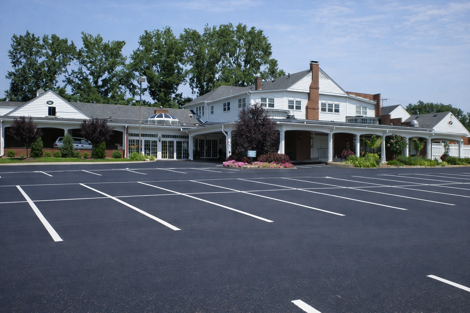 Empty parking lot in front of a white building with a covered porch and trees behind it