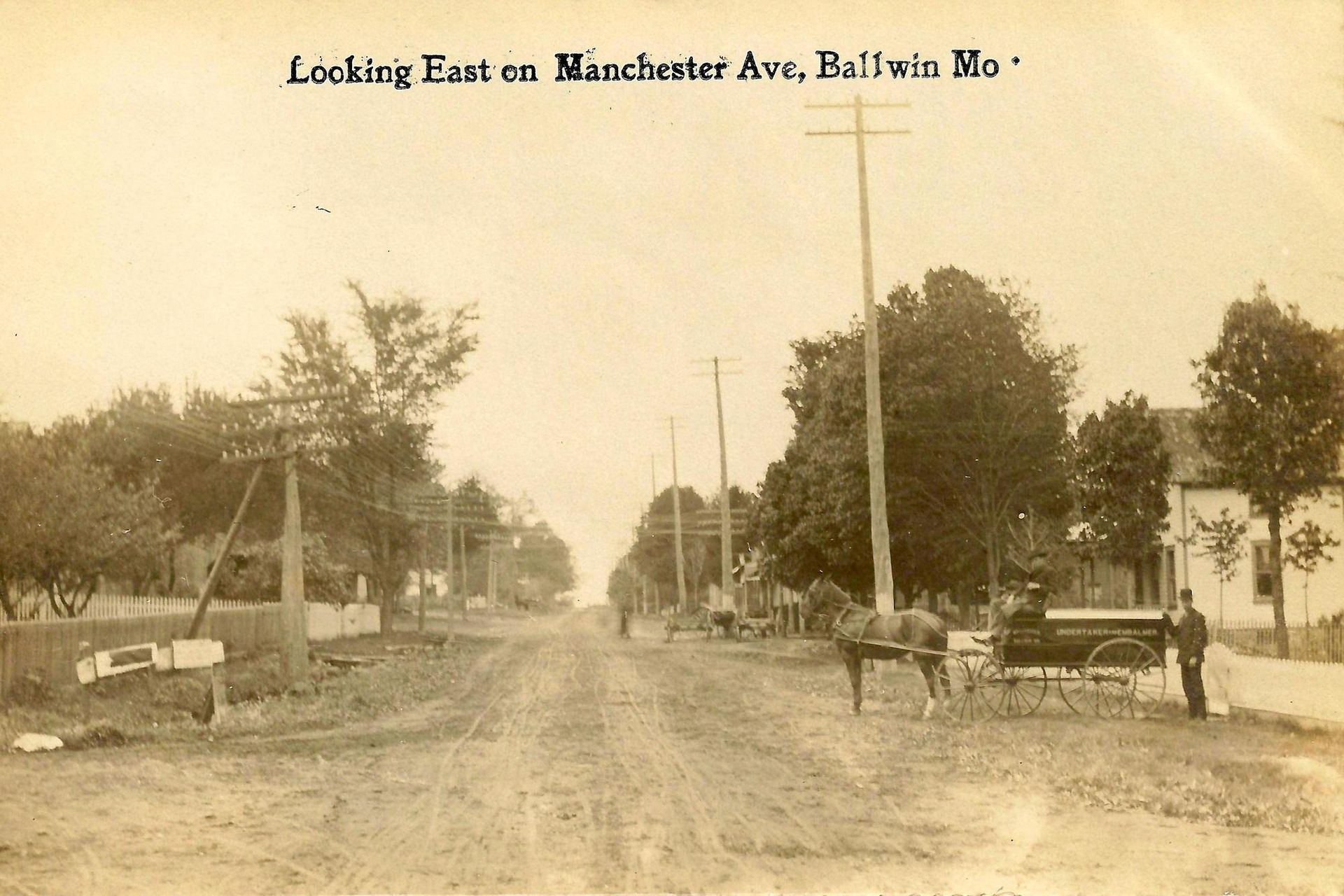 Sepia street view of Manchester Ave. in Baldwin, Missouri, with dirt road and horse-drawn carts.