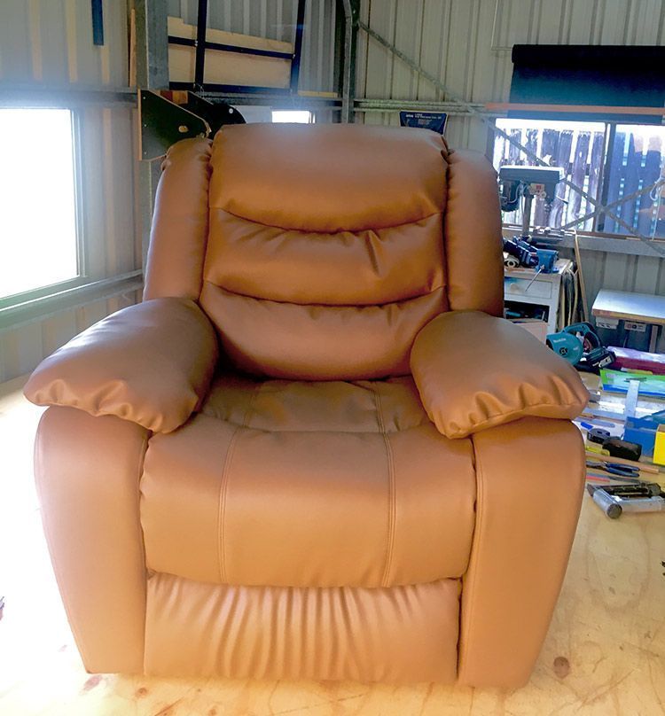 A Brown Leather Recliner is Sitting on a Wooden Floor in a Room — Paulie's Upholstery in Edmonton, QLD