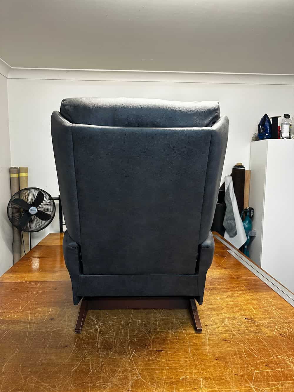 A Black Leather Recliner Is Sitting In A Room Next To A Fan — Paulie's Upholstery in Edmonton, QLD