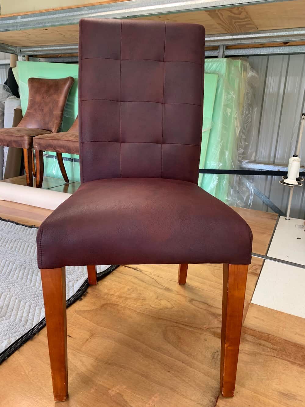 A Brown Chair With Wooden Legs Is Sitting On A Wooden Floor — Paulie's Upholstery in Edmonton, QLD