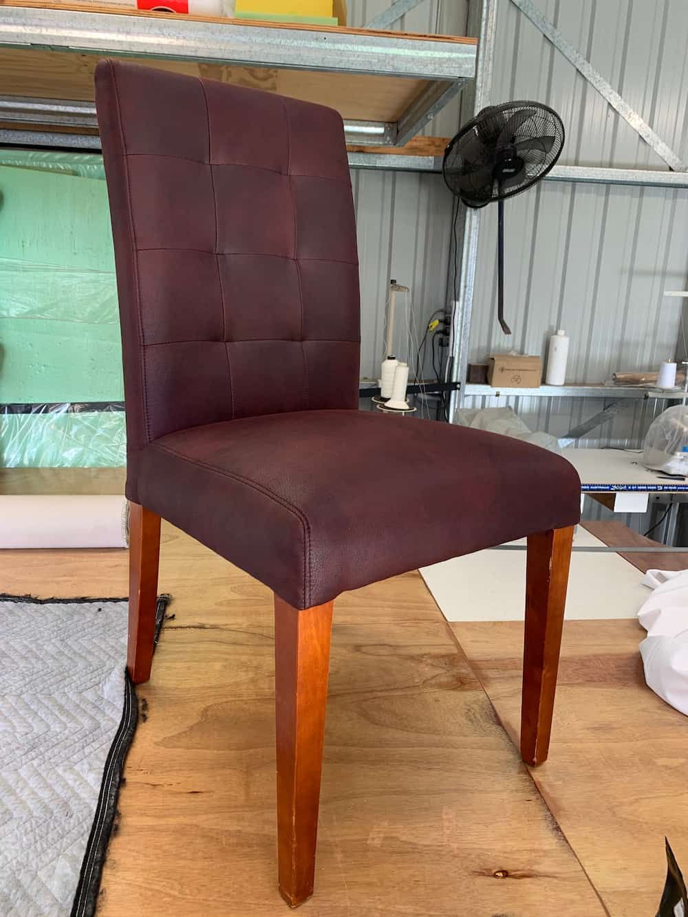 A Chair Is Sitting On A Wooden Floor Next To A Fan — Paulie's Upholstery in Edmonton, QLD
