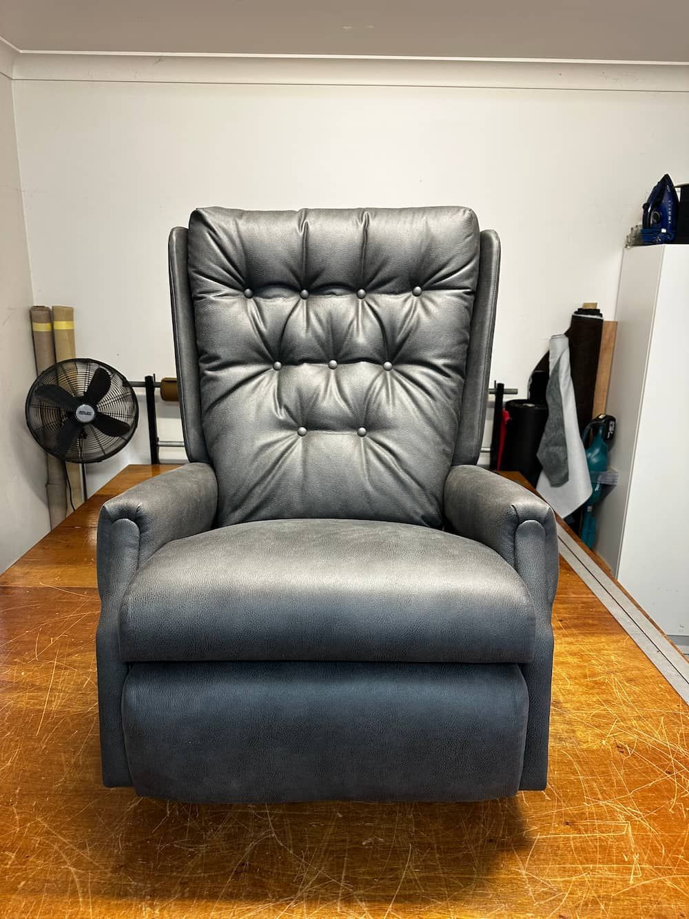 A Black Leather Recliner Is Sitting In A Room Next To A Fan — Paulie's Upholstery in Edmonton, QLD