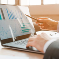 A person in a suit points to a laptop screen displaying various business charts and data analysis.