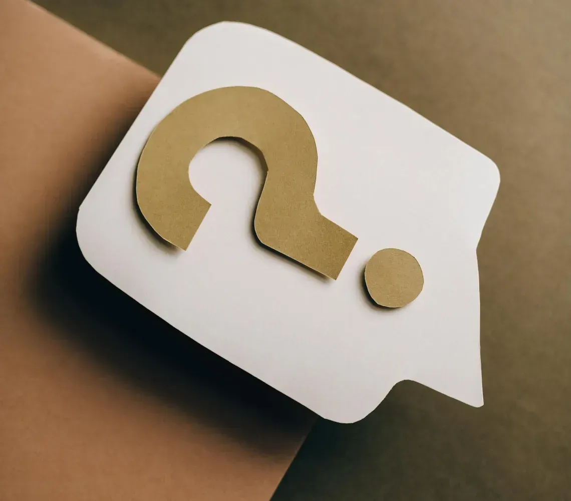A wooden mannequin hand holds a small card with a question mark on it against a black background.