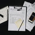 A black desk with a 2023 calendar, IRS tax forms on a clipboard, a calculator, a pen, and a magnifying glass.