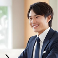 A professional in a suit smiles while sitting at a desk opposite a client in a bright, modern office setting.