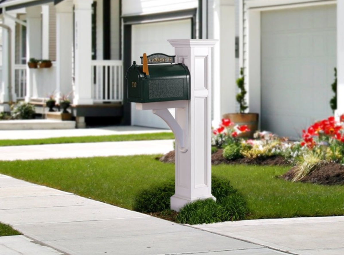 White mailbox on a suburban sidewalk beside a row of houses and flower beds