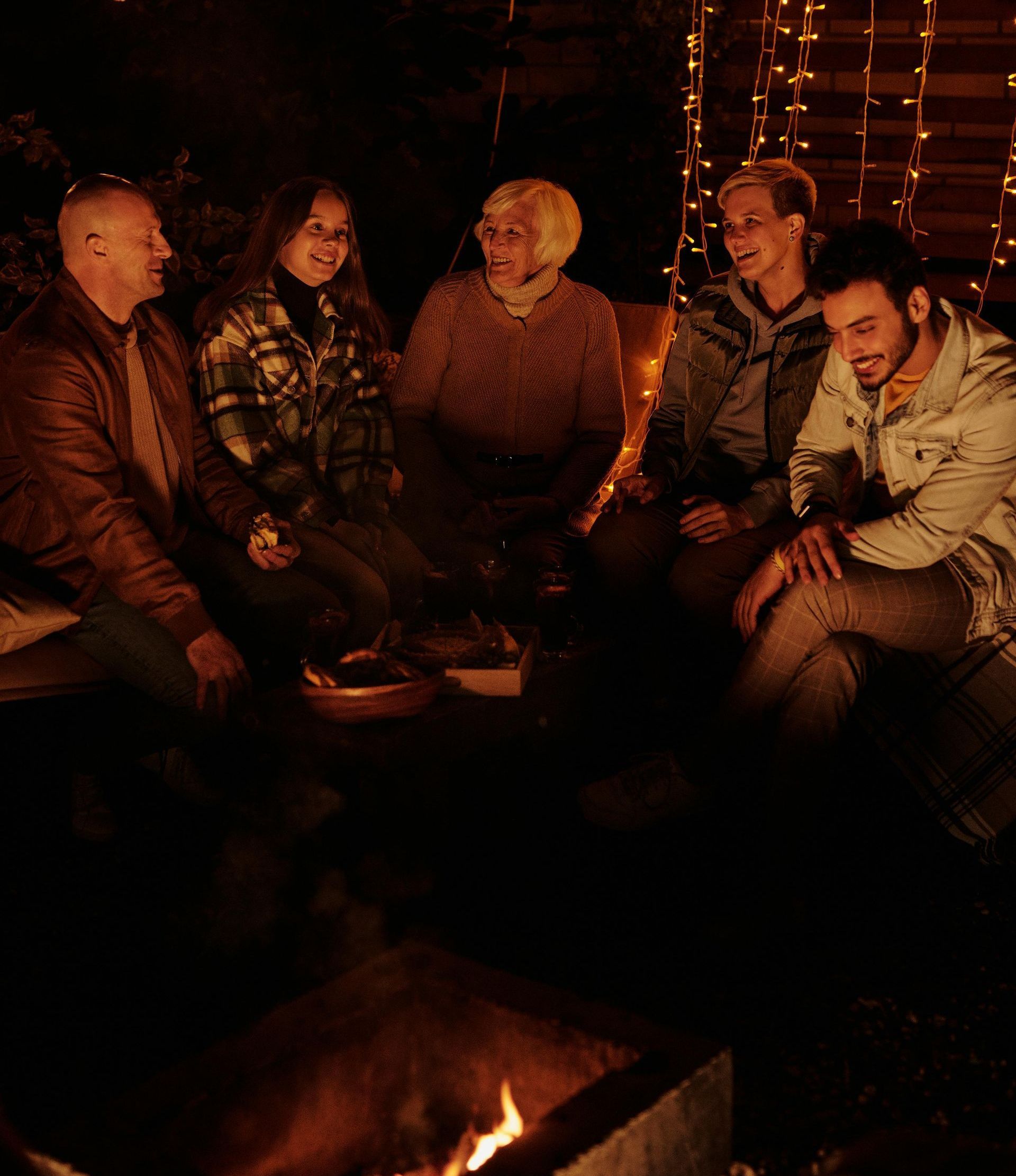 A group of people are sitting around a fire pit at night.