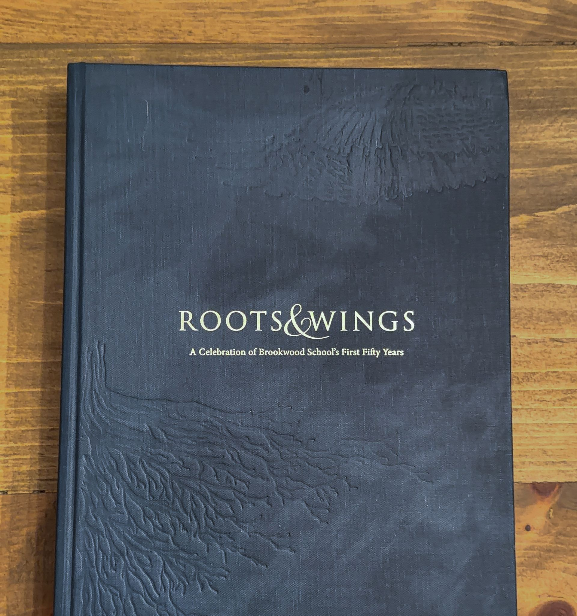 Black book titled “ROOTS & WINGS” on a wooden surface