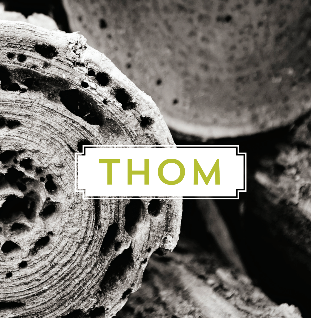 Close-up black-and-white textured wood with a white label reading “THOM” in yellow-green text