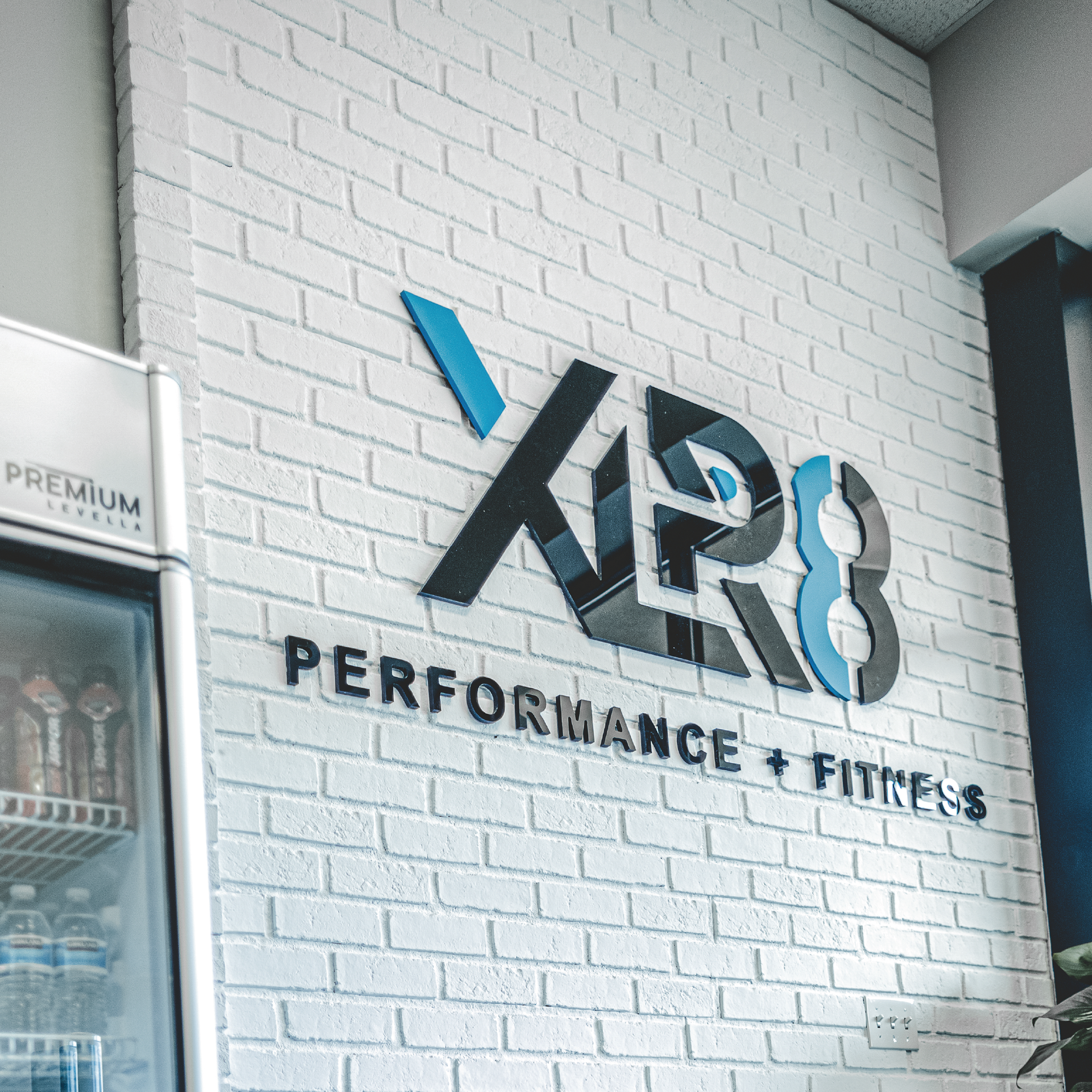 X28 Performance + Fitness logo on a white brick wall in a gym entrance