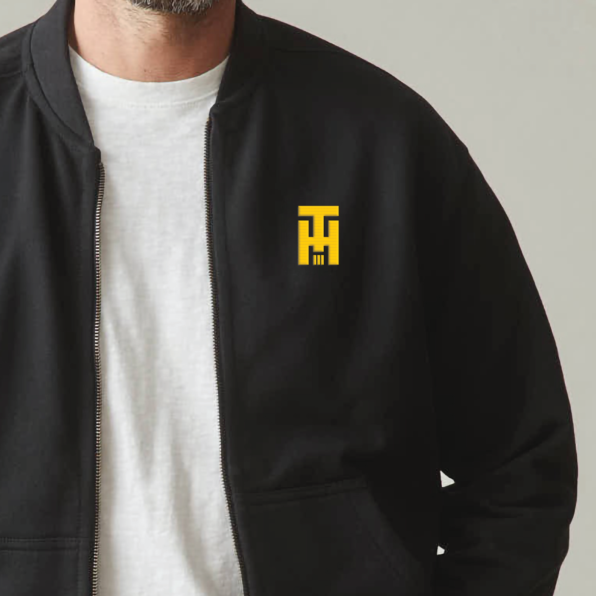 Black jacket with yellow logo over a white T-shirt, shown on a person against a neutral background