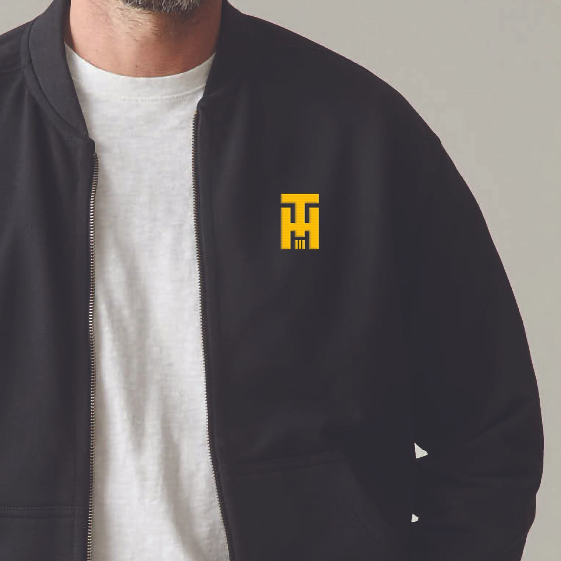 Close-up of a person wearing a black jacket with a yellow logo over a white T-shirt.