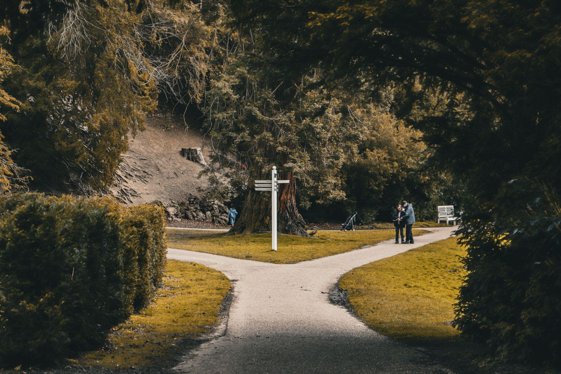 Forked garden path with a white cross monument and two people walking in the distance