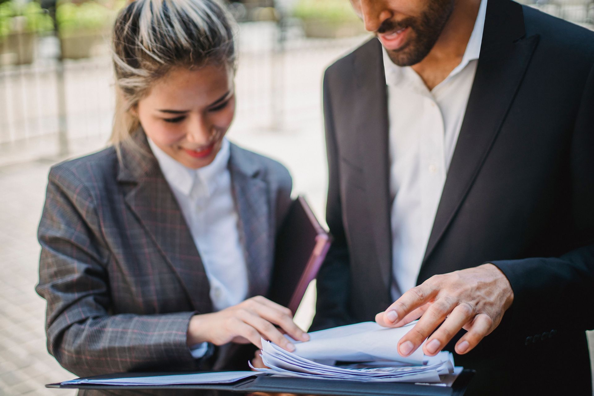 Two professionals reviewing documents together outdoors, one pointing at papers on a table.