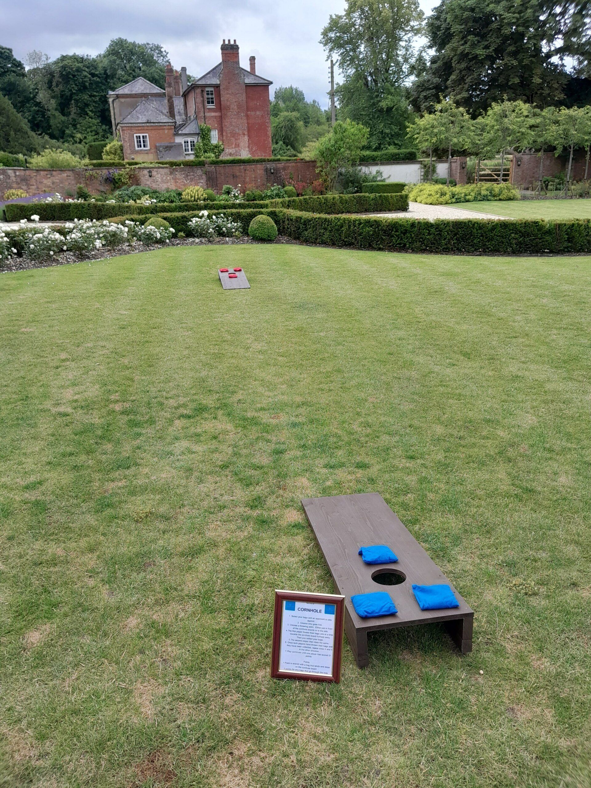 2 Wooden Cornhole lawn game with 3 bean bags and an information sign on grass at a hotel