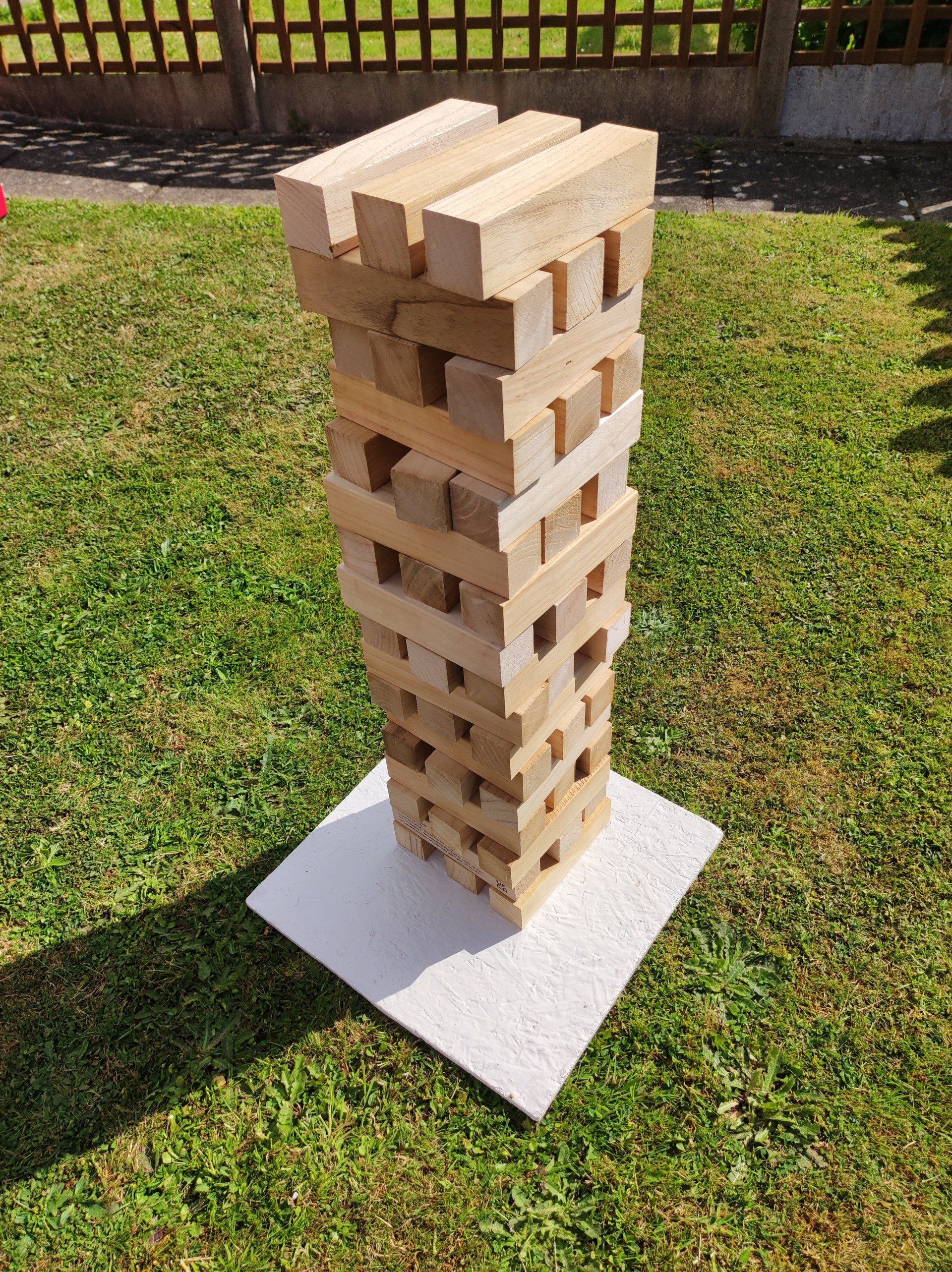 Giant wooden jenga set up on a white board on green grass.