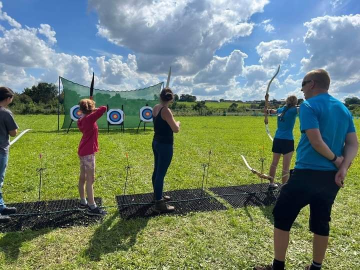 3 archery targets with safety net. 4 people shooting and an instructor watching