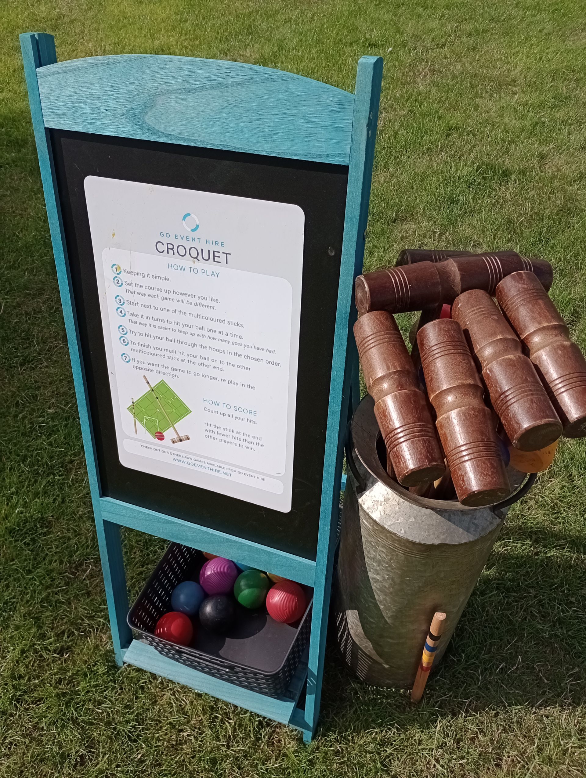 Croquet information sheet on a blackboard A frame next to croquet clubs in a milk urn.